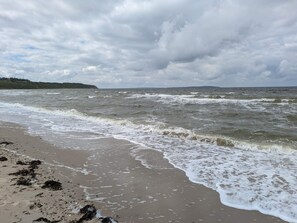 A beach with waves, a cloudy sky, and a distant landmass. - Holiday Home in Ranum (Ranum)