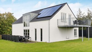 Une maison moderne à deux étages, dotée d’un balcon, de panneaux solaires et d’un jardin clôturé.