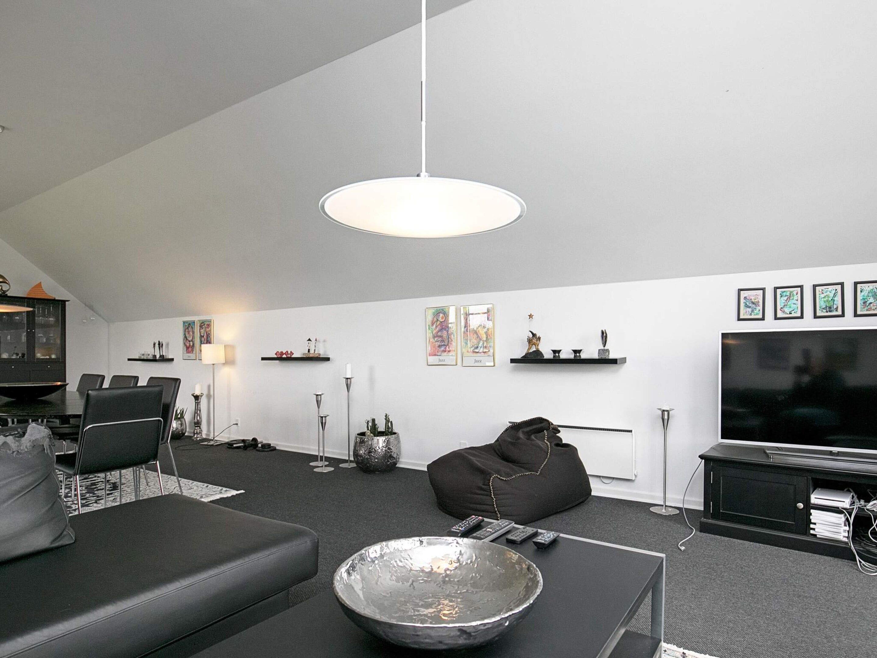 A modern living room with a dining area, a black sofa, a coffee table, a TV, and artwork on the walls.