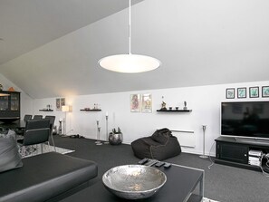 A modern living room with a dining area, a black sofa, a coffee table, a TV, and artwork on the walls. - Holiday Home in Ranum (Ranum)