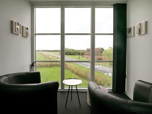 A room with a large window, two black leather chairs, a small round table, and artwork on the walls.