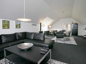 A modern living room with a black leather sofa, a coffee table with a bowl and remotes, and a dining area with chairs and a table. - Holiday Home in Ranum (Ranum)