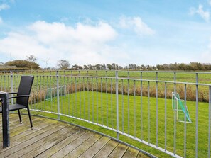 A wooden deck with a metal railing, a black chair, and a view of a green field with wind turbines in the distance.