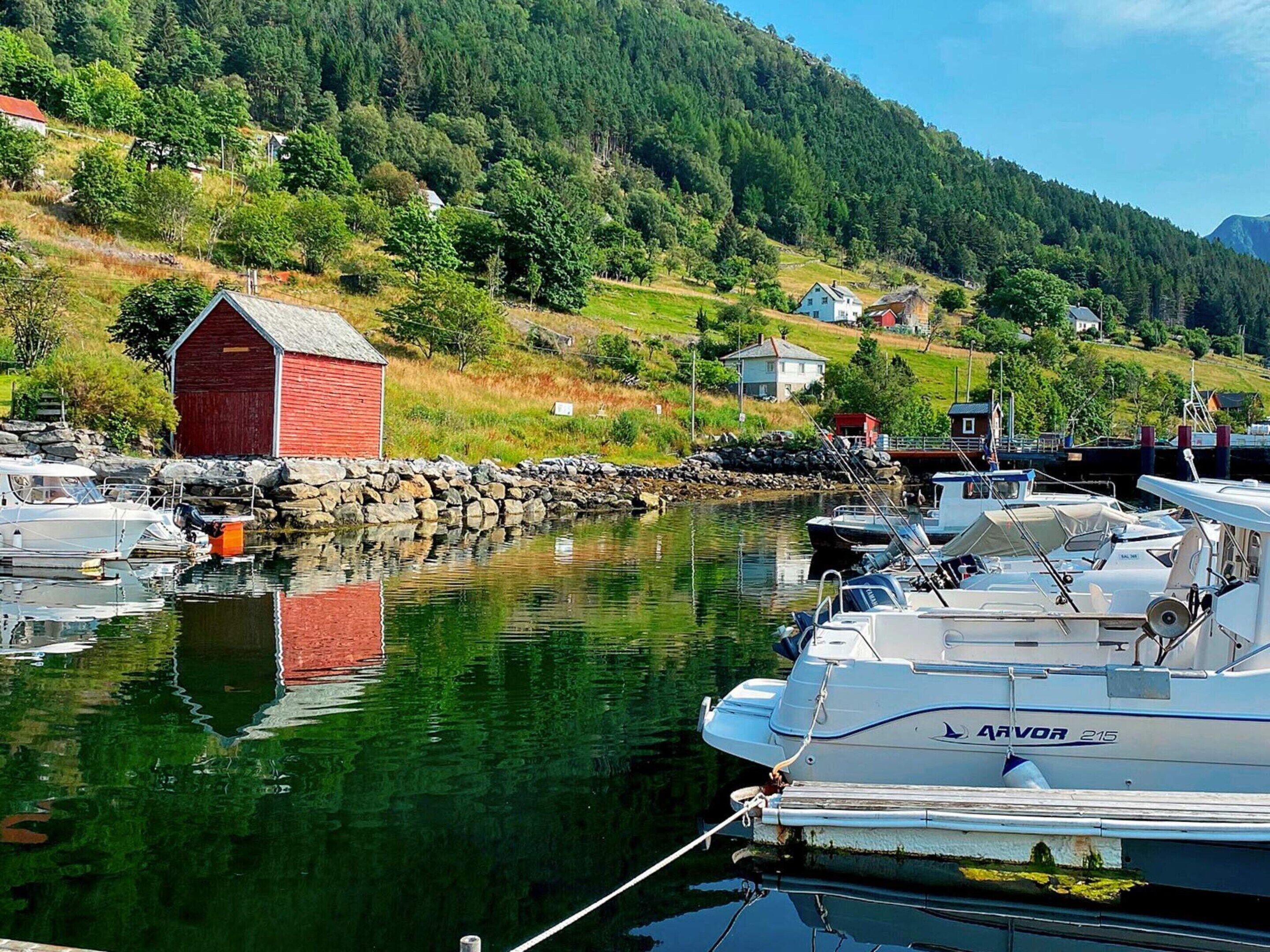 En småbåtshamn med förtöjda båtar, en röd byggnad och hus i bakgrunden.