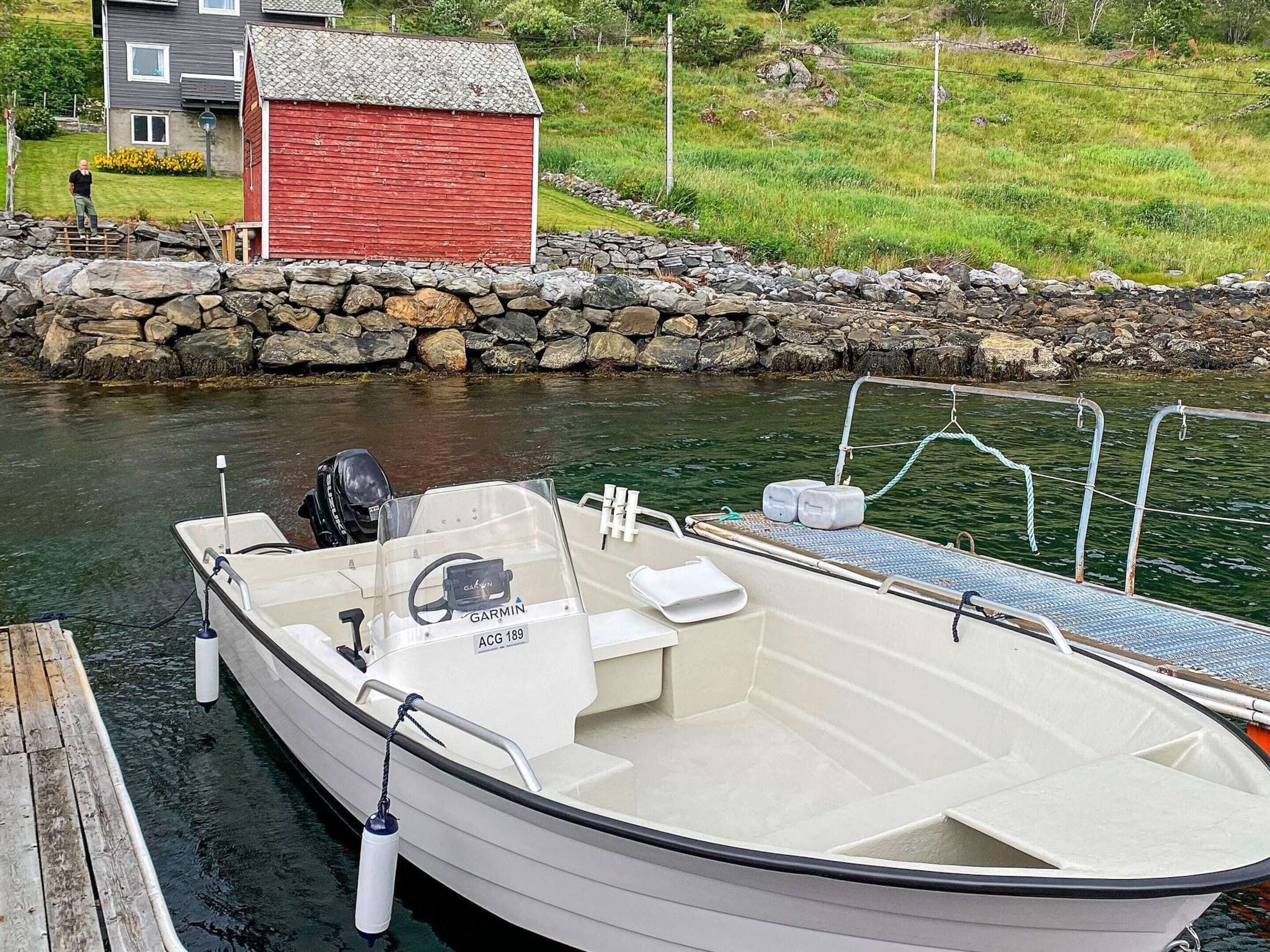 A small white boat docked at a pier with a Garmin navigation system, a white cabin, and a red building in the background.