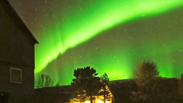 A house with a visible garage and a lit window, under a night sky with the aurora borealis. - 6 Person Holiday Home in Storsteinnes (Balsfjord)