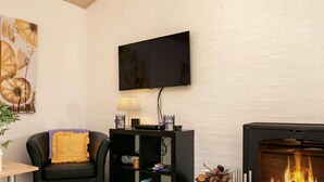 Una sala de estar con un sofá de cuero negro, un televisor de pantalla plana montado en la pared, una chimenea con leña y una estantería con diversos objetos.