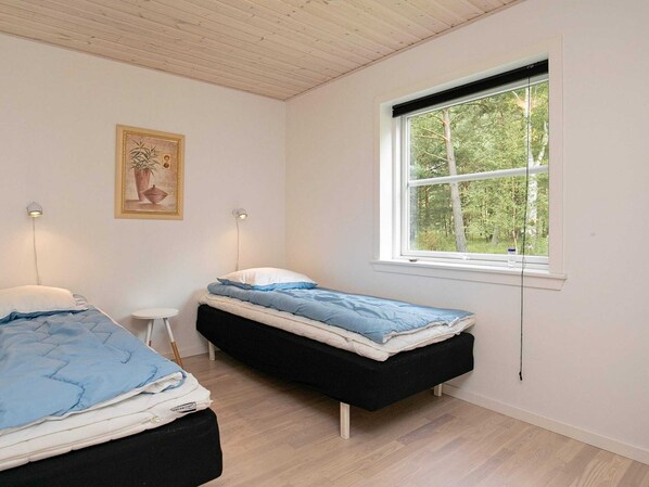 A small, clean room with two beds, a window with a view of trees, and a painting on the wall.