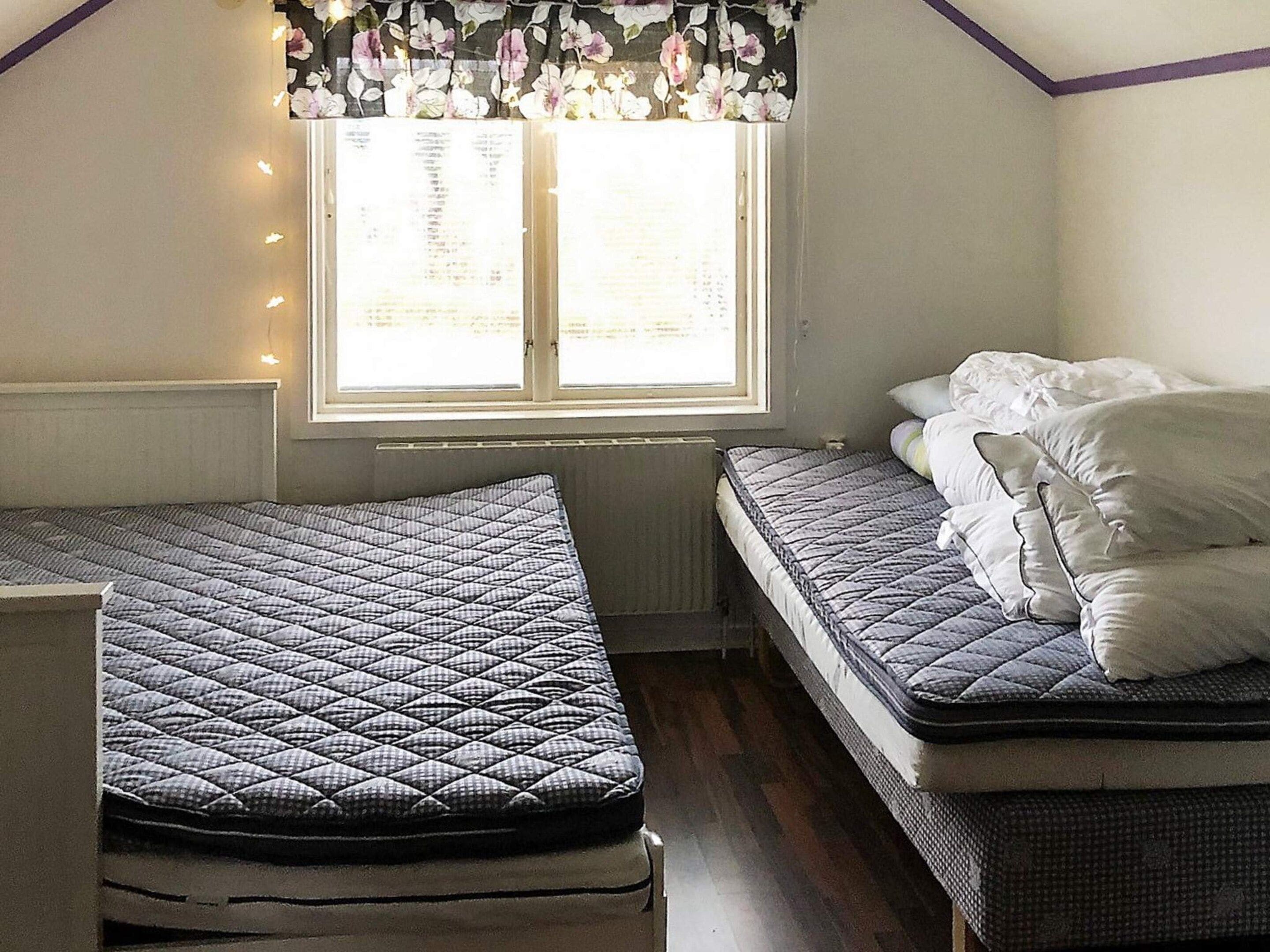 A room with two beds, a window with a floral curtain, and a radiator.