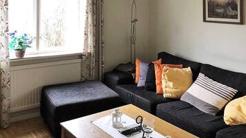 Una sala de estar con sofá, reposapiés y una mesa de centro con un control remoto y un vaso.