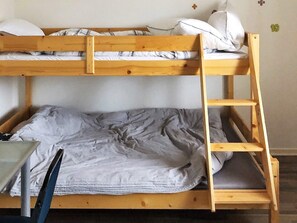 Un lit superposé avec une structure en bois, une literie grise et une petite table avec une chaise.