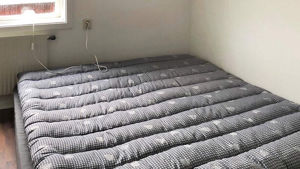A compact, rectangular bed with a checkered pattern and leaf designs, in a room with a window and electrical outlets. - 10 Person Holiday Home in Karbole (Kårböle)