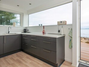 A modern kitchen with a large window, dark cabinetry, and a wooden floor.