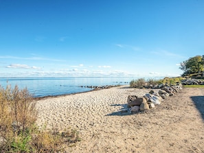 A sandy beach with a clear blue sky, a calm sea, and a row of rocks.