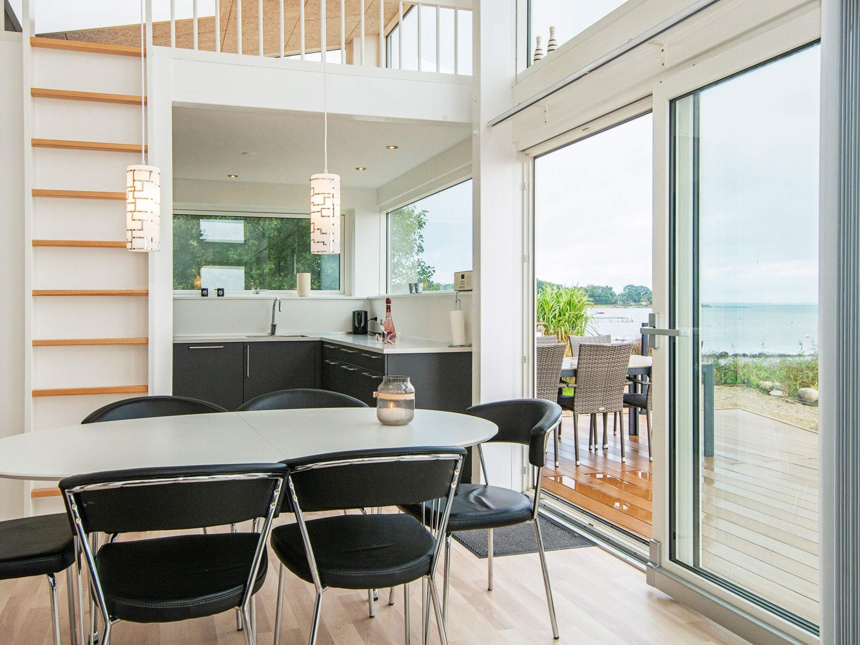 Una cocina moderna con una isla grande, un comedor con sillas negras y vista al mar.