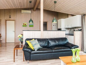 Una sala de estar moderna con un sofá de cuero negro, una mesa de centro de madera y una zona de cocina con armarios blancos y encimera negra.