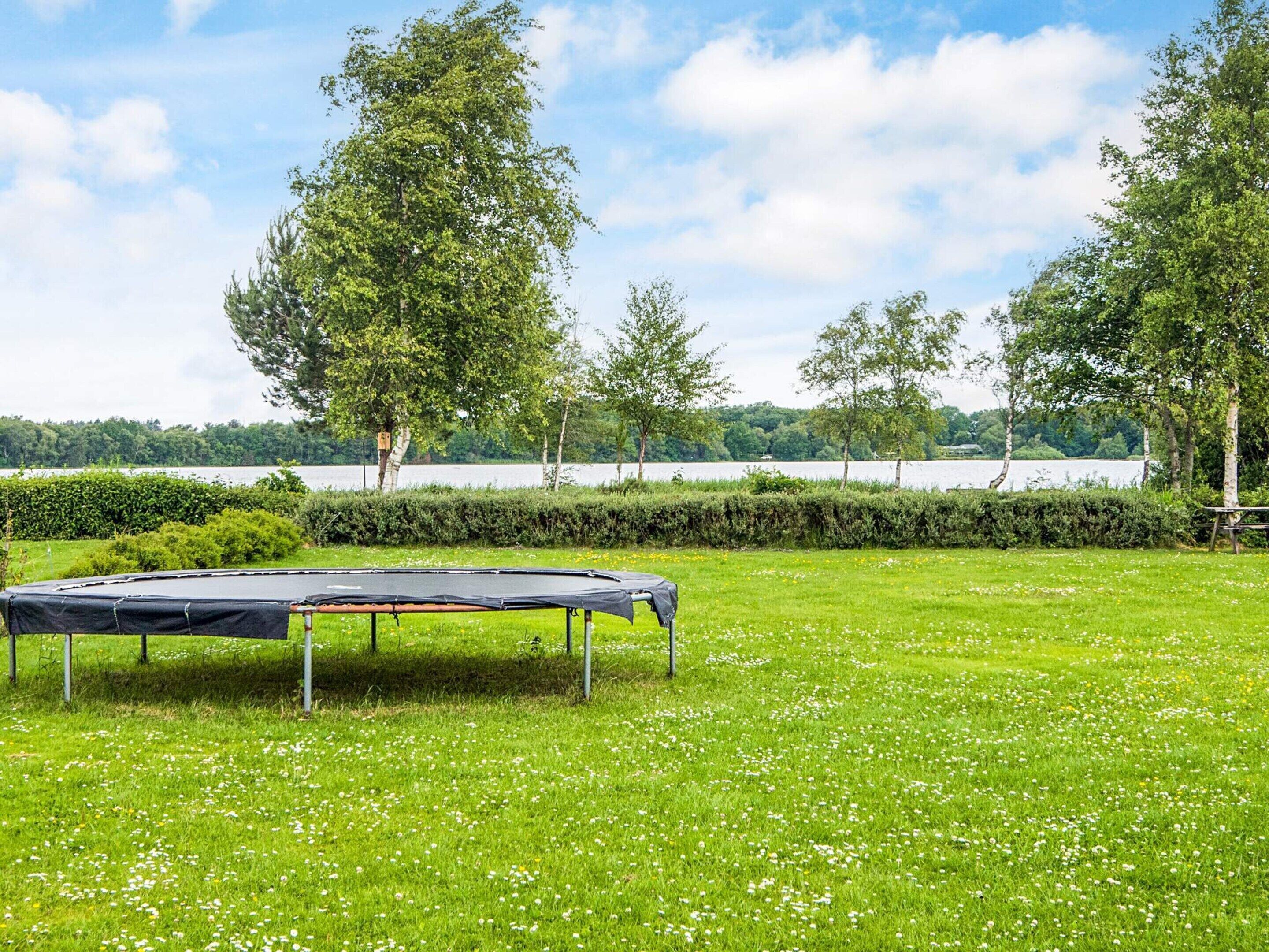 A trampoline in a grassy field with trees and a body of water in the background.