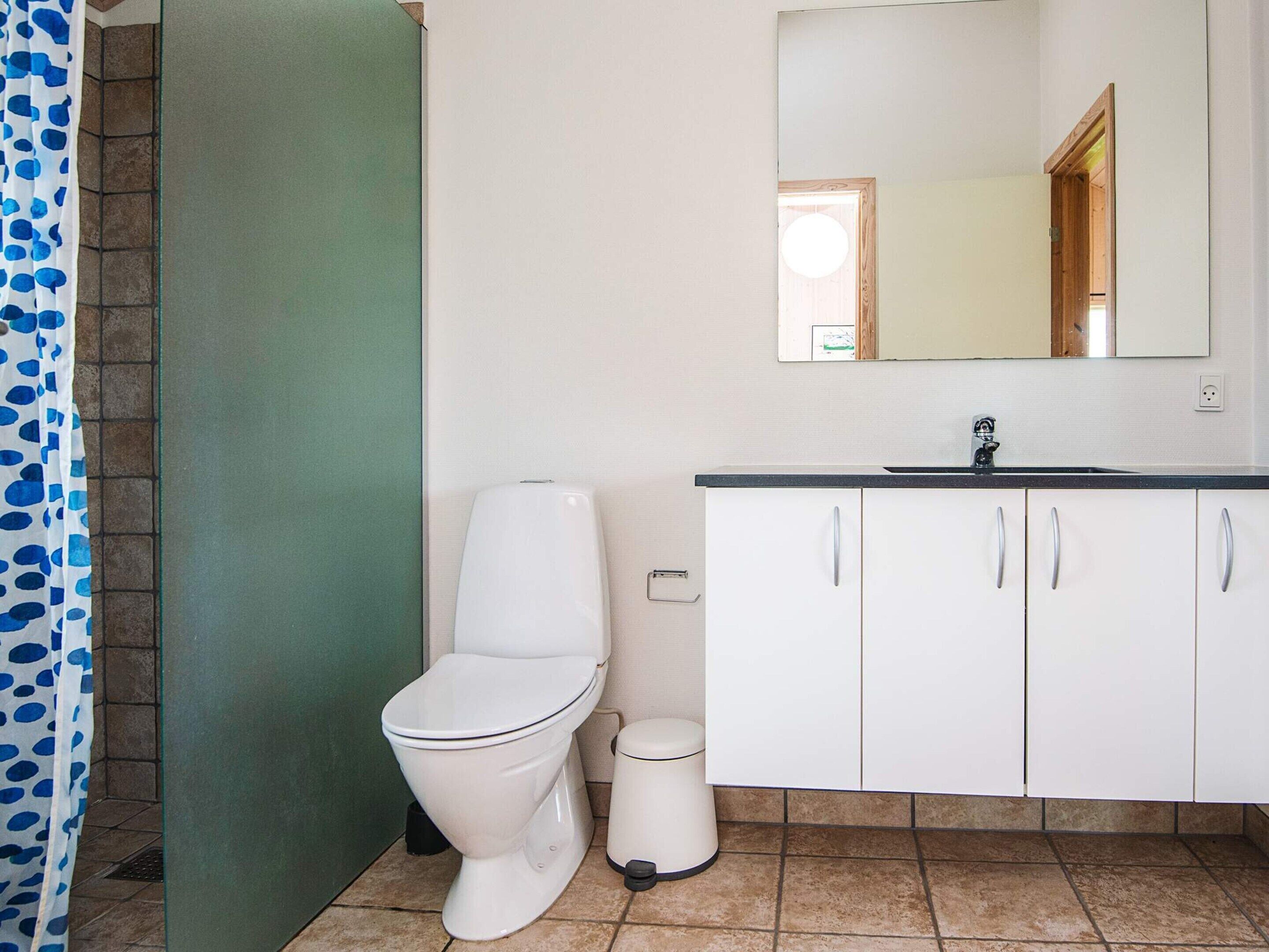 Un baño con inodoro, un cubo de basura, un lavabo con espejo y armarios.
