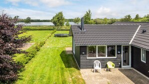 Una casa moderna con techo oscuro, ventanas amplias y un patio con dos sillas.