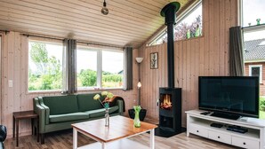 Una sala de estar acogedora con un sofá verde, una mesa de centro de madera, un mueble para la televisión y una estufa de leña.