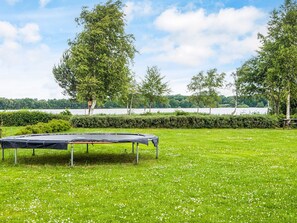 Un trampolín en un campo cubierto de césped, con árboles y una masa de agua al fondo.