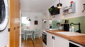 A compact kitchen with white cabinetry, a wooden countertop, a built-in oven, and a sink. There is a dining area with a table and chairs, and a clock on the wall. - 6 Person Holiday Home in Børkop (Borkop)