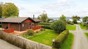 A single-story wooden house with a red door and a small porch, surrounded by a well-maintained lawn and a gravel driveway. - 6 Person Holiday Home in Børkop (Borkop)