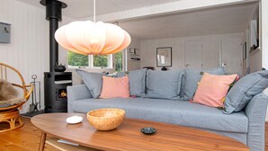 A cozy living room with a gray sofa, a wooden coffee table, a wicker chair, and a black wood-burning stove. - 6 Person Holiday Home in Børkop (Borkop)