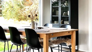 Uma área de refeições com mesa de madeira, cadeiras pretas e um aparador de vidro com louças.