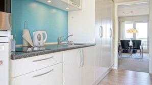 Una cucina moderna con mobili bianchi, una parete di colore blu e un'area pranzo con tavolo e sedie.