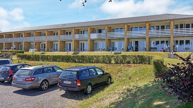 A multi-story hotel with a flat roof and a row of balconies. There are several cars parked in front, and the hotel has a well-maintained lawn and hedges.