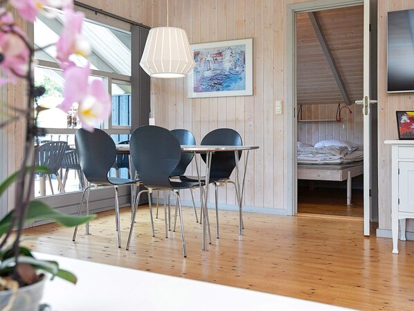 A room with a dining table, chairs, a bed, a TV, and a painting on the wall.