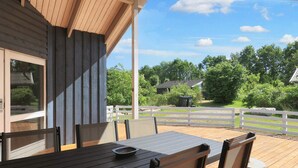 A wooden deck with a table and chairs, a white fence, and a view of greenery and houses in the background.