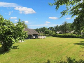 A grassy yard with a building that has a sloped roof and an air conditioning unit. There are trees and a fence in the background. - 6 Person Holiday Home in Vaeggerlose (Vaeggerlose)