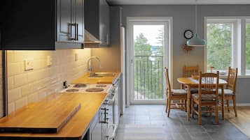 Une cuisine moderne avec un plan de travail en bois, des appareils en acier inoxydable et un coin repas comprenant des chaises et une table en bois.