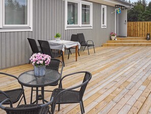 Un patio exterior con una mesa redonda y sillas, una mesita con un florero y una terraza de madera.