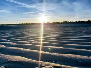 A beach with a sun reflecting on the wet sand, creating a pattern of light and shadow.