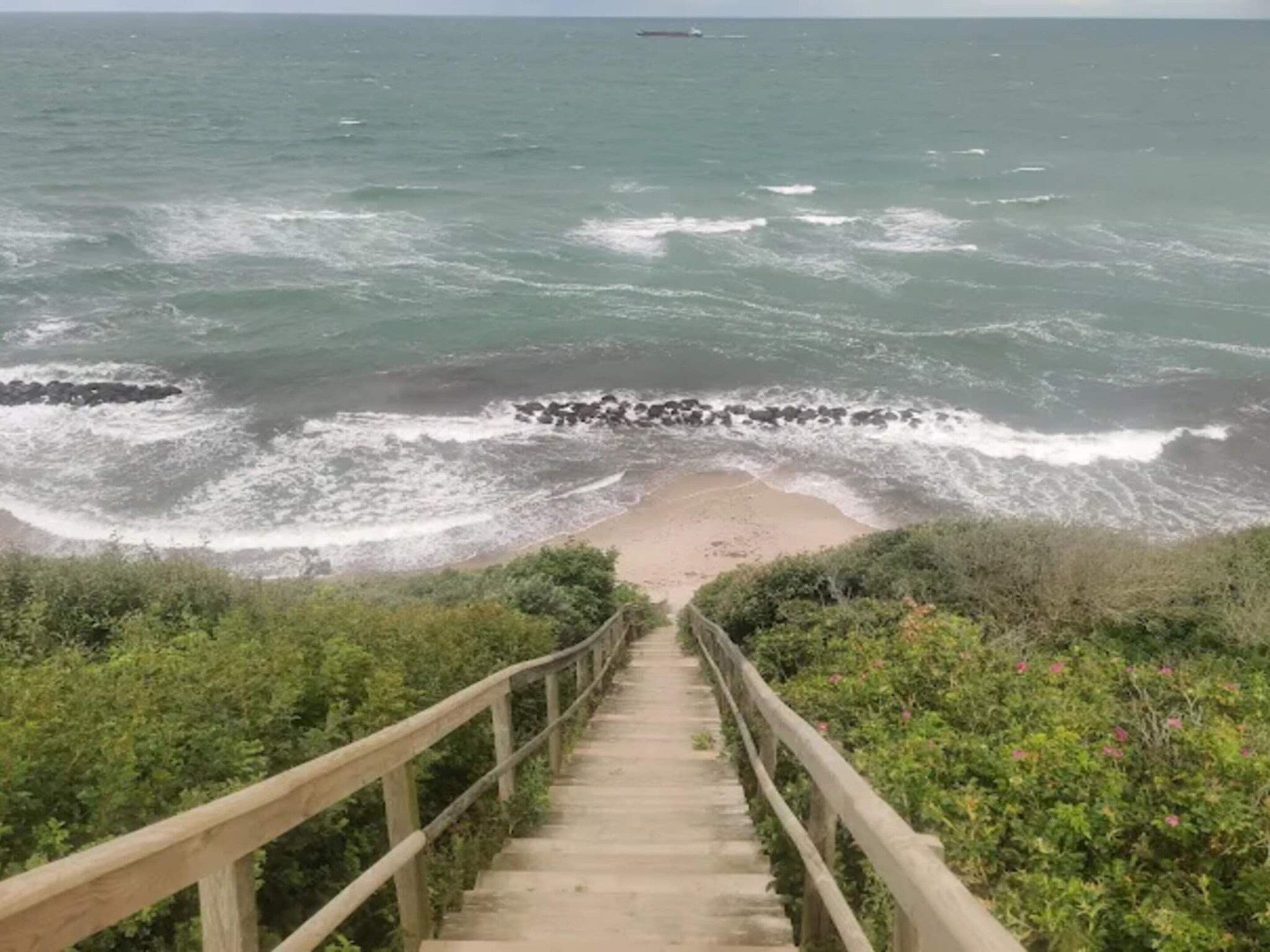 A concrete staircase leading down to a beach with waves crashing onto the shore.