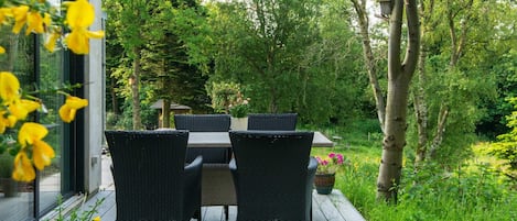 Un espace de restauration en plein air, avec une table et des chaises, entouré de verdure et d’arbres.