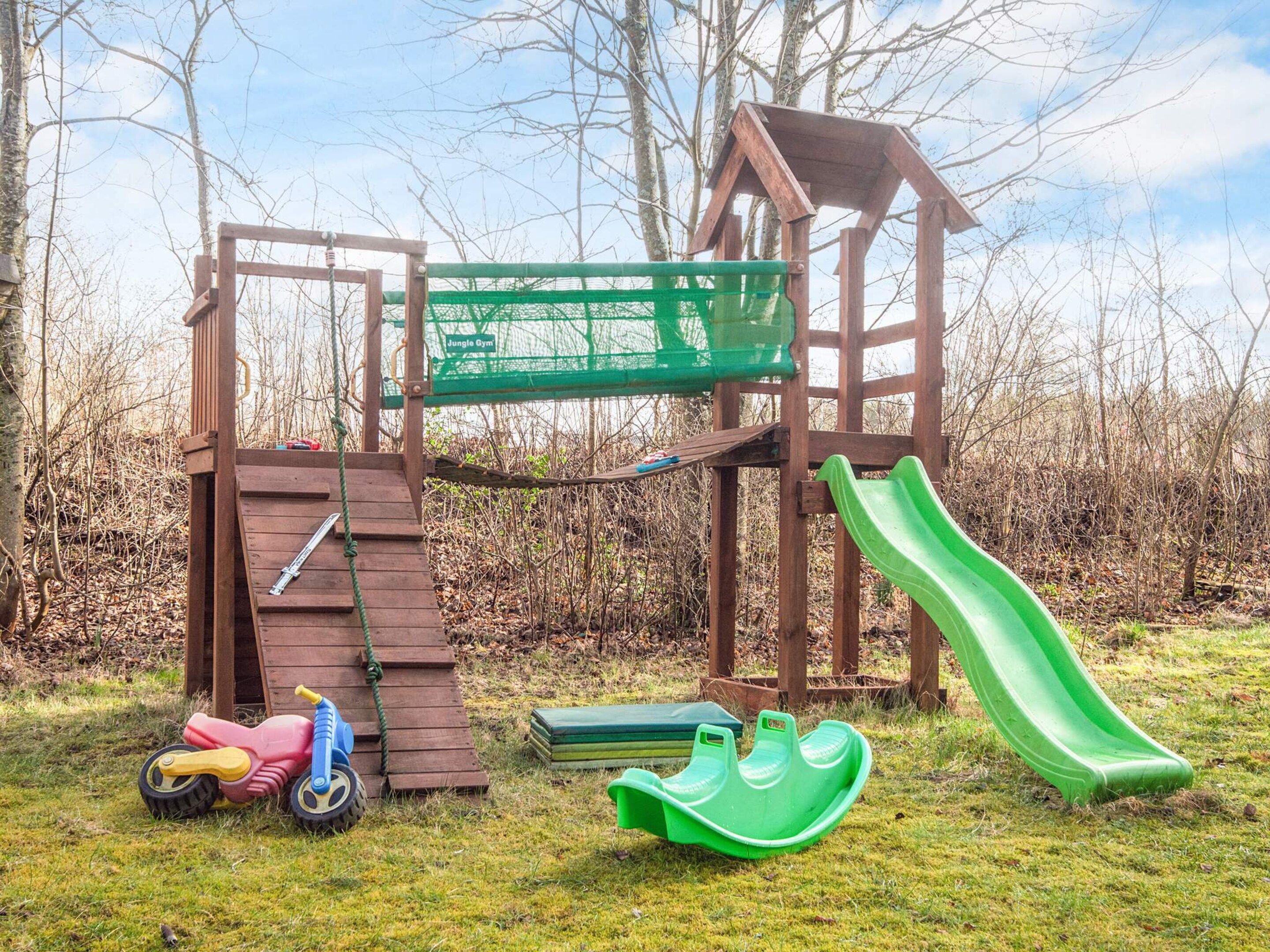 Eine Holzspielkonstruktion mit Rutsche, Kletternetz und einem kleinen, grünen Boot.