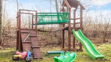 Eine Holzspielkonstruktion mit Rutsche, Kletternetz und einem kleinen, grünen Boot.