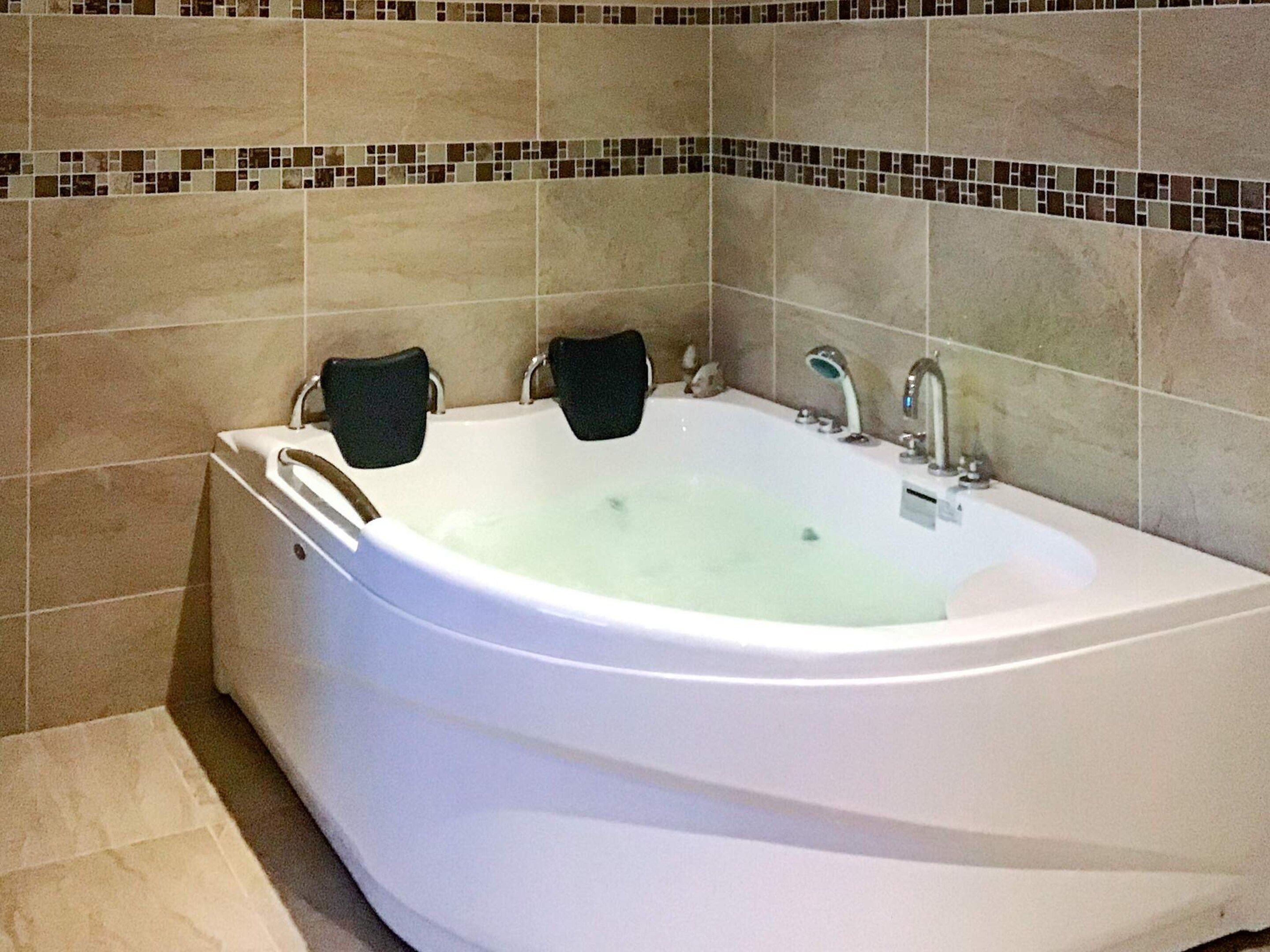 A large, white freestanding bathtub with two black towels, set against a tiled wall with a mosaic border.