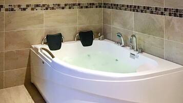 A large, white freestanding bathtub with two black towels, set against a tiled wall with a mosaic border.
