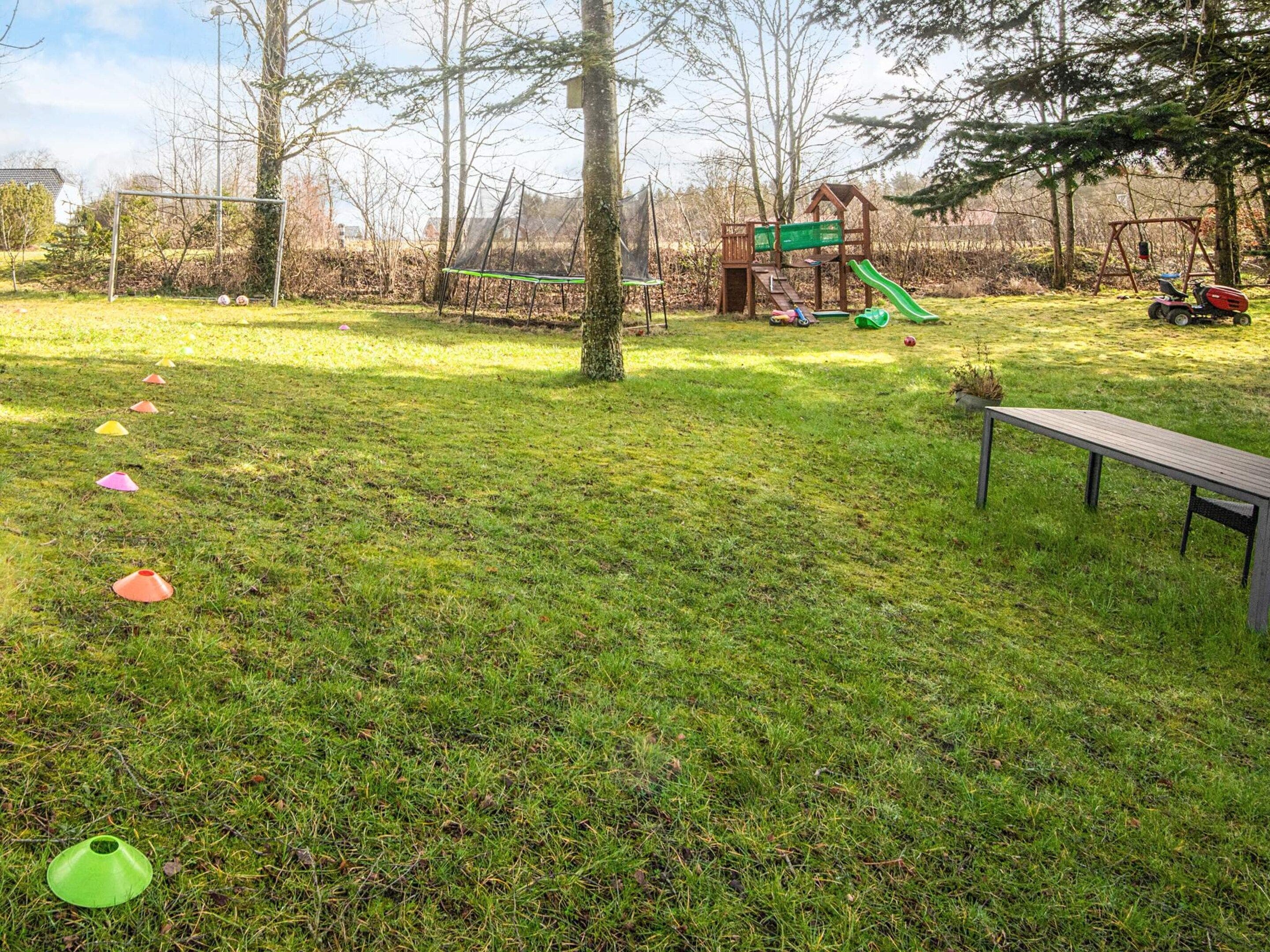 Ein Rasenbereich im Freien mit einem Spielplatz, darunter eine Rutsche und Schaukeln, sowie eine Bank.
