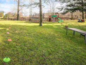 A grassy outdoor area with a playground, including a slide and swings, and a bench. - Holiday Home in Holstebro (Holstebro)