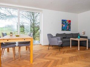 Un salon moderne comprenant un coin repas, un canapé gris, une table basse et un tableau coloré accroché au mur.