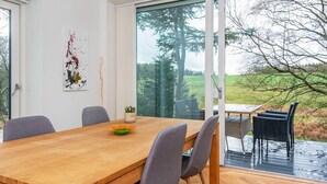 Ein Essbereich mit einem Holztisch, vier grauen Stühlen und Blick auf einen Garten durch eine Glastür.