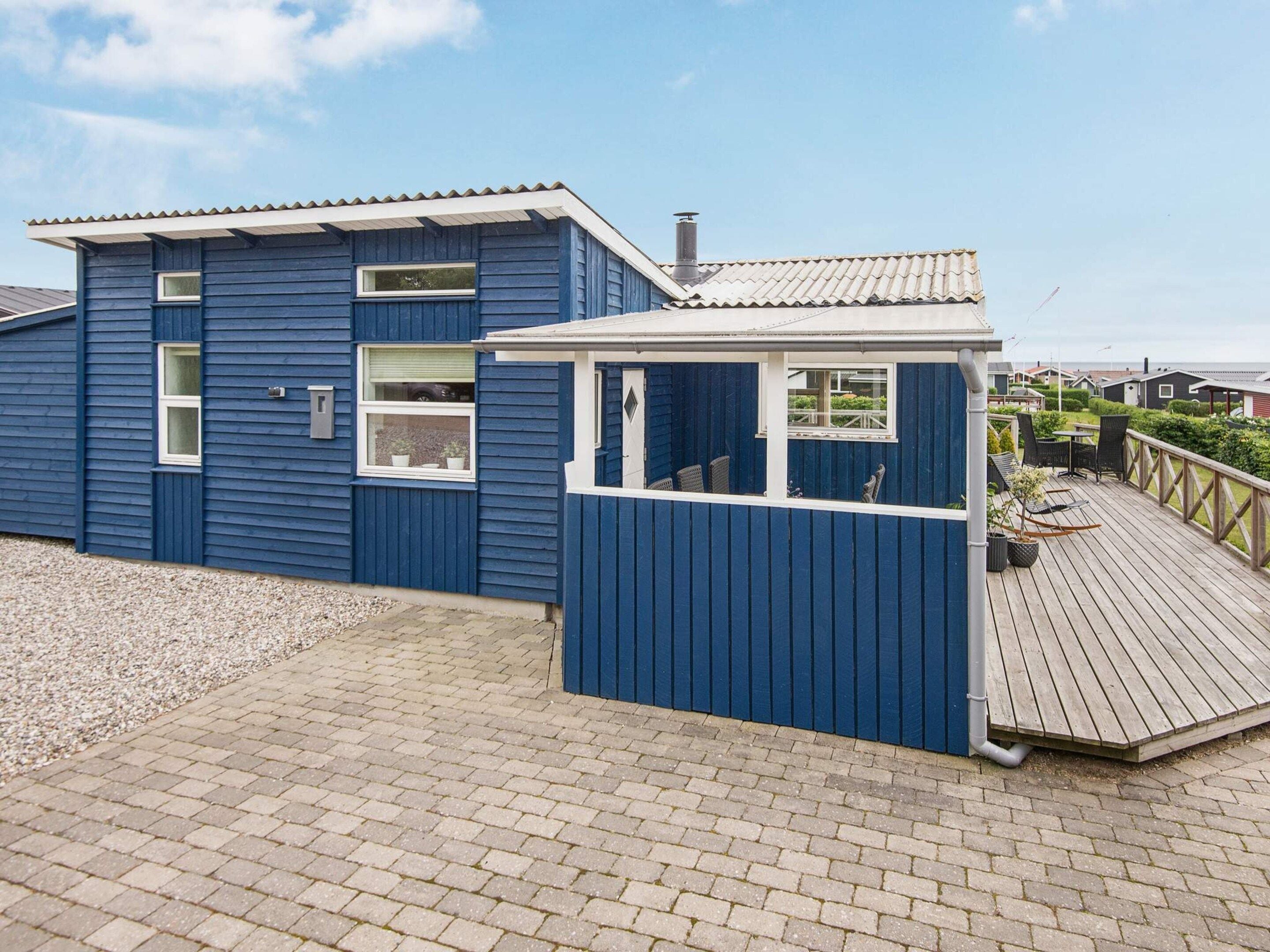 A blue wooden building with a balcony, a small porch, and a gravel pathway.