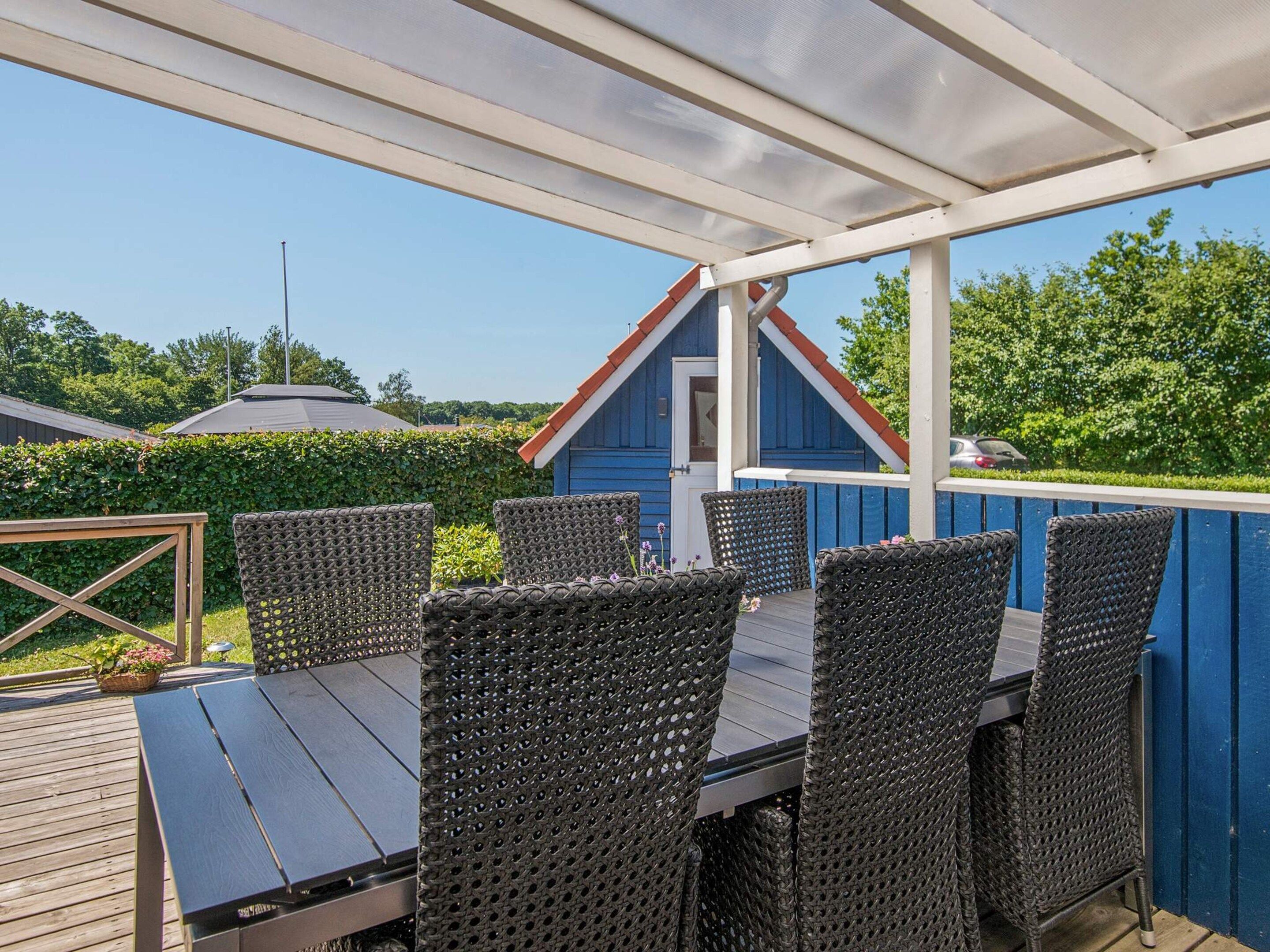 An outdoor patio with a table and chairs, a blue building in the background, and a clear sky.