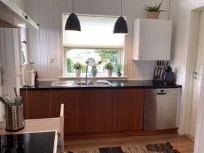 A modern kitchen with wooden cabinets, a black countertop, a built-in dishwasher, and a window with potted plants.